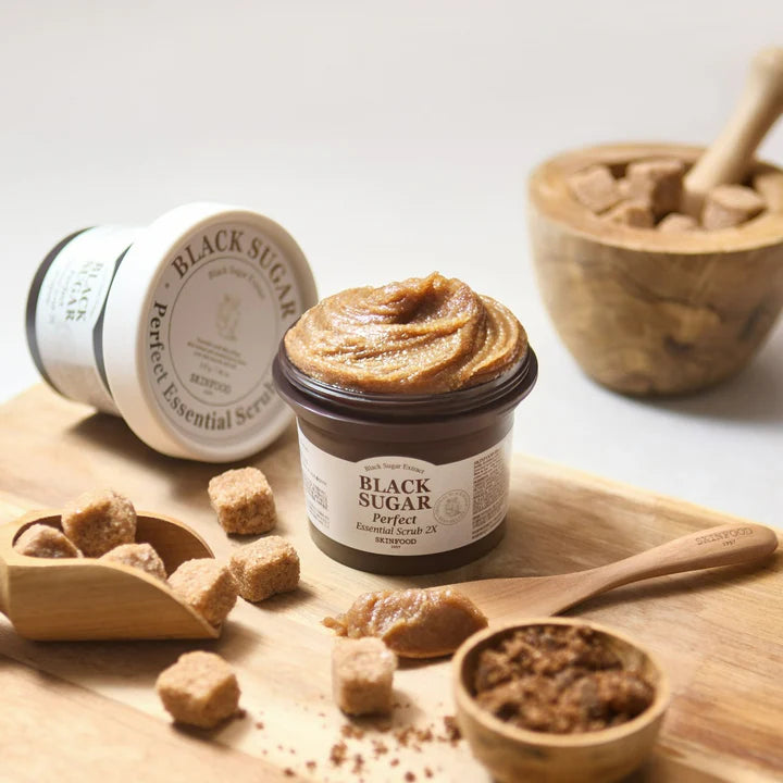 SKINFOOD Black Sugar Perfect Essential Scrub 2X with sugar cubes on a wooden board and a spoon.