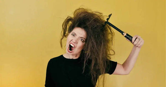 Person with frizzy hair using a curling iron, expressing frustration to get rid of frizzy hair.