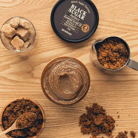 SKINFOOD Black Sugar Perfect Essential Scrub 2X in a jar with brown sugar and sugar cubes on a wooden surface.
