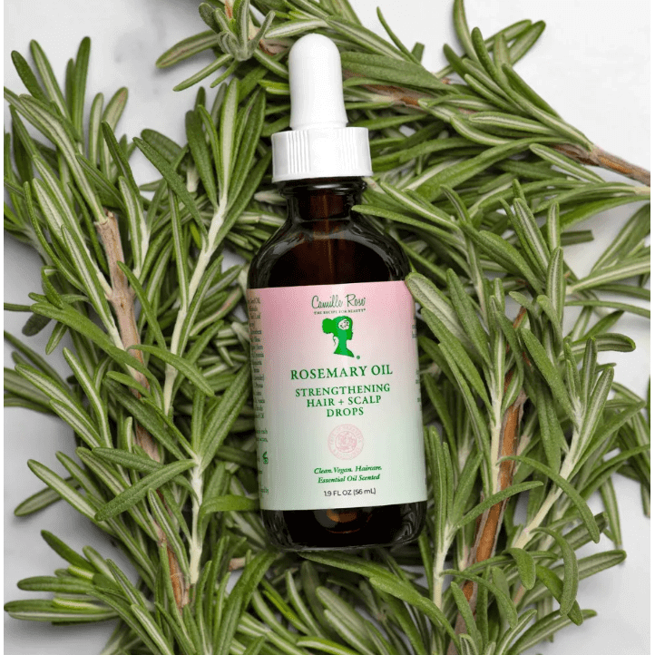Camille Rose Rosemary Oil Strengthening Hair Drops displayed on fresh rosemary leaves.