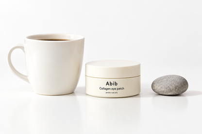 Illustrative image of an ABIB Collagen Eye Patch Jericho Rose Jelly jar beside a cup and stone.