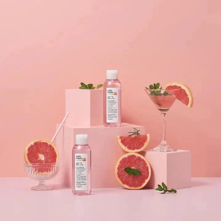 SKINFOOD Pink Grapefruit AHA Toner 200ml displayed with fresh grapefruits in a vibrant pink setting.